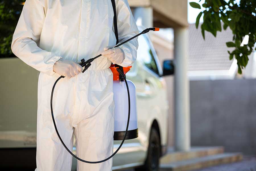 A person in white suit holding a sprayer.
